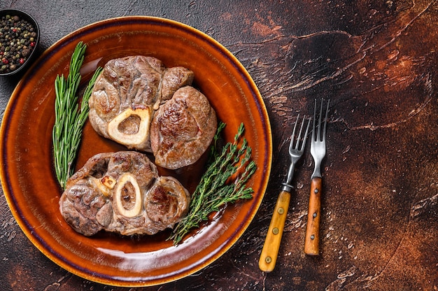 Gekochtes Fleisch am Knochen Osso Buco Kalbshaxe, italienisches Ossobuco Steak. Dunkler hölzerner Hintergrund. Ansicht von oben. Platz kopieren.