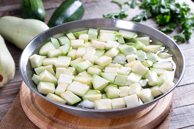 Gekochtes Gemüse, Zucchini in einem Sieb in Eiswasser nach dem Blanchieren. Tiefkühlkost-Konzept.