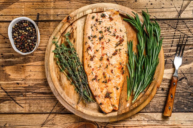 Gekochtes Lachsfilet mit Kräutern und rosa Pfeffer. hölzerner Hintergrund. Draufsicht.