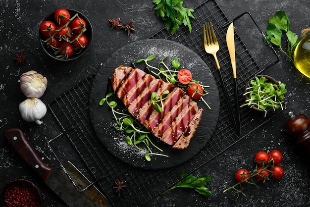 Gekochtes saftiges Thunfischsteak mit Gemüse auf einer schwarzen Steinplatte Essen im Restaurant Meeresfrüchte Rustikaler Stil flach gelegt