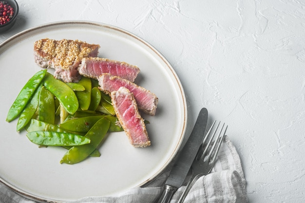 Foto gekochtes thunfischsteak in sesam, besetzt mit frühlingszwiebeln und zuckerschoten, auf teller, auf weißem stein