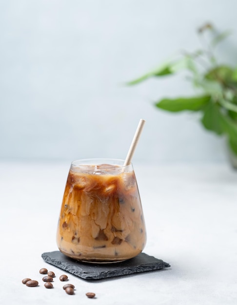 Gekühlter Kaffeelatte in einem Glas mit Milch auf einem hellen Hintergrund mit Kaffeebohnen und Blättern