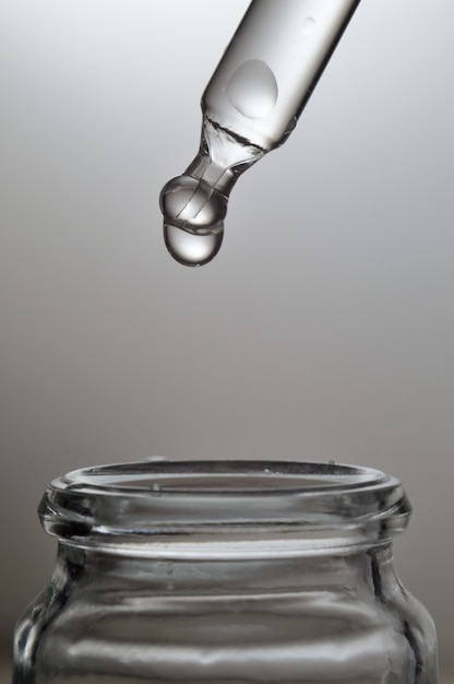 Gel líquido transparente ou pipeta de soro com gotas em fundo cinza.
