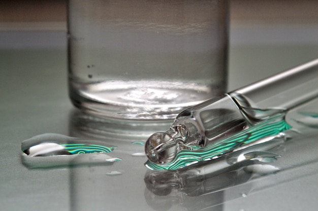Gel líquido transparente ou pipeta de soro com gotas no fundo de vidro.