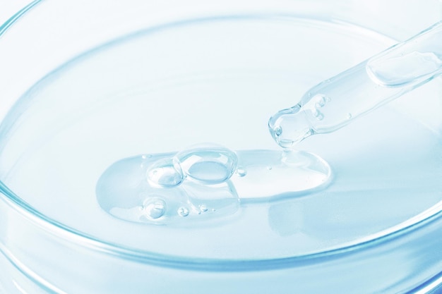 Gel transparente que fluye de una pipeta a una placa de Petri Sobre un fondo azul Primer plano