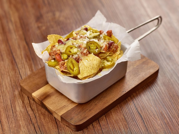 Geladene Nachos-Chips mit geschmolzenem Käse und Chili in einer Schüssel isoliert auf dunklem Holztisch Seitenansicht Singapur Essen