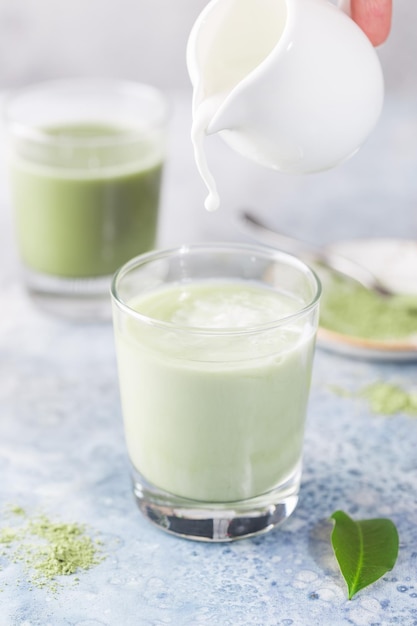 Gelado com leite matcha verde em copos com pó matcha sobre fundo claro.