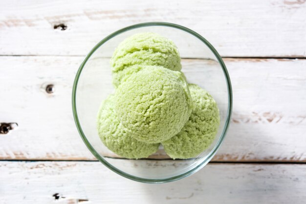 Gelado de chá verde matcha colheres na tigela de cristal na vista superior de mesa de madeira branca