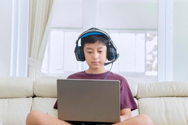 Gelangweilter jugendlicher Junge, der zu Hause einen Laptop verwendet