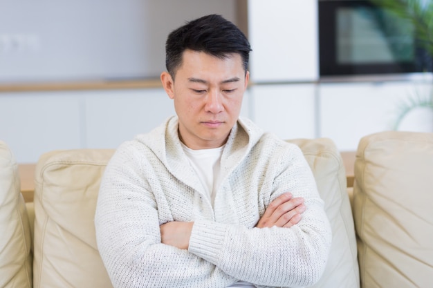 gelangweilter junger asiatischer Mann, der allein zu Hause auf dem Sofa sitzt