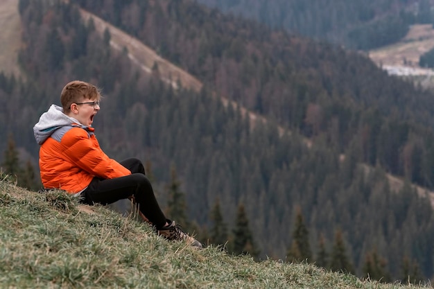 Gelangweilter Kerl sitzt am Hang und gähnt Junge schreit in den Bergen Porträt des Kindes im Herbst auf Wanderung