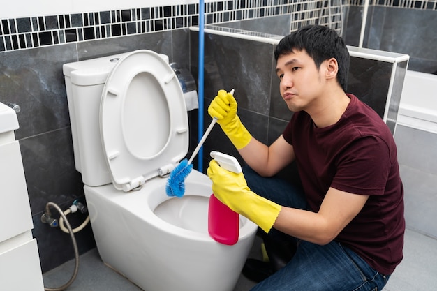 Gelangweilter Mann, der Toilettenschüssel im Badezimmer reinigt