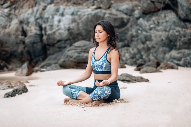 Gelassene östliche Frau meditiert in Lotus-Pose am Sandstrand bei den Felsen.