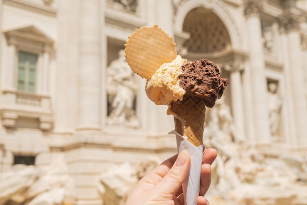 Gelato é sorvete italiano Casquinha de sorvete na mão de uma mulher contra o pano de fundo da Fonte de Trevi Sorvete de baunilha de chocolate com um círculo de waffle