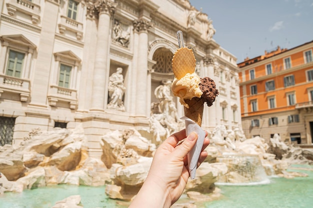 Gelato es helado italiano Cono de helado en la mano de una mujer contra el telón de fondo de la Fontana de Trevi Helado de vainilla de chocolate con un círculo de gofres