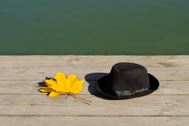 Gelbe Ahornblätter und schwarzer Hut auf dem Pier