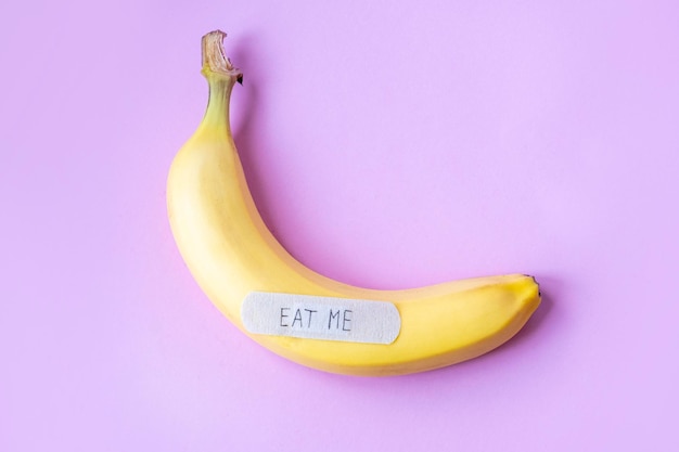 Gelbe Banane mit Gipsnote EAT ME auf pinkfarbenem Hintergrund Minimales Food-Konzept Flache Ansicht von oben