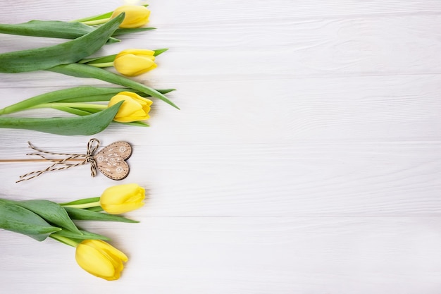 Gelbe Blumen Tulpen und Holzherz auf einem Stock mit einer Schleife