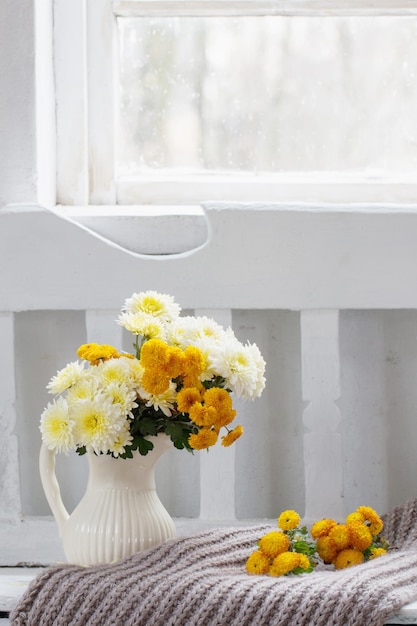 Gelbe Chrysanthemen im Krug auf alter weißer Holzbank