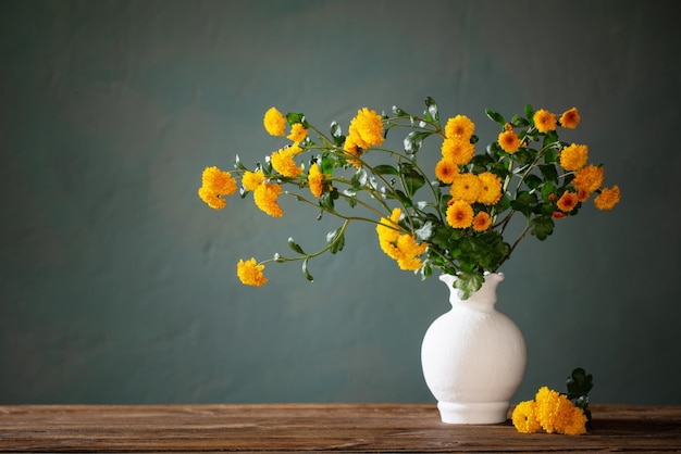 gelbe Chrysanthemen in weißer Vase auf dunkler Wand im Hintergrund