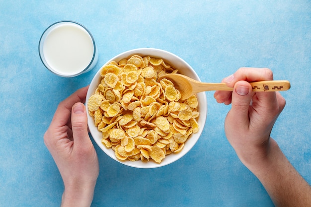 Gelbe Corn Flakes und ein Glas Milch zum trockenes gesundes Frühstück. Ansicht von oben. Getreidelöffel und -schüssel in den Händen