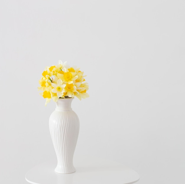 Gelbe Frühlingsblumen in weißer Vase auf weißem Hintergrund