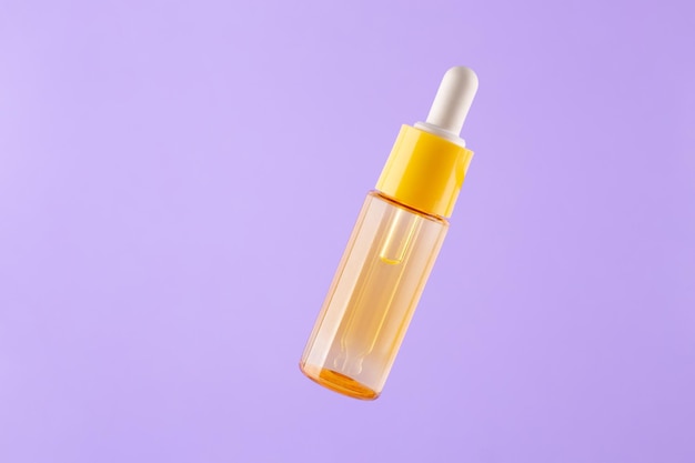 Gelbe Glasflasche mit Pipette mit ätherischem Öl auf violettem Hintergrund Draufsicht Aromatische Kosmetik