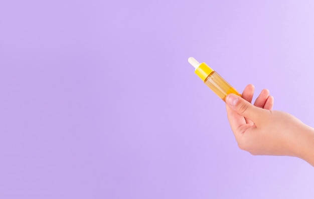 Gelbe Glasflasche mit Pipette mit ätherischem Öl in weiblicher Hand auf Draufsicht des purpurroten Hintergrundes