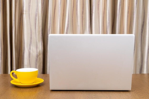 Gelbe Kaffeetasse und Laptop-Computer auf Holztisch