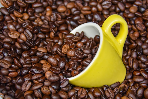 Gelbe Kaffeetassen und Arabica-Kaffeebohnen, die bis zum Mahlen wärmebehandelt wurden.