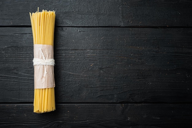 Gelbe lange Spaghetti, gelbe italienische Pasta, auf schwarzem Holztischhintergrund, Draufsicht flach liegend, mit Copyspace und Platz für Text