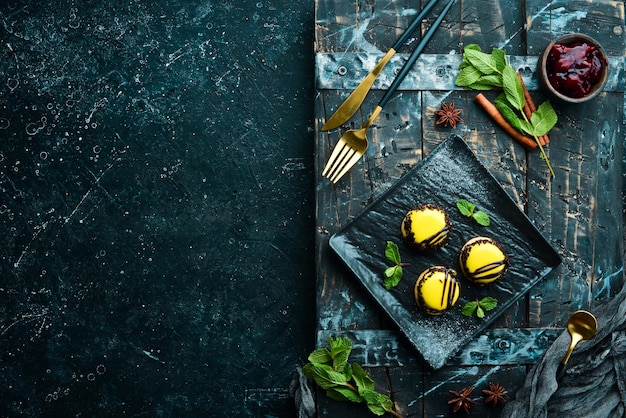 Gelbe Mango-Desserts Makronen auf einem schwarzen Teller mit Minze Draufsicht Rustikaler Stil