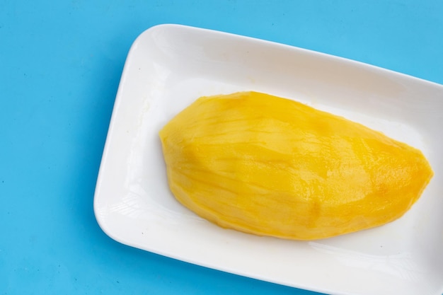 Gelbe Mangoscheiben in weißer Platte auf blauem Hintergrund