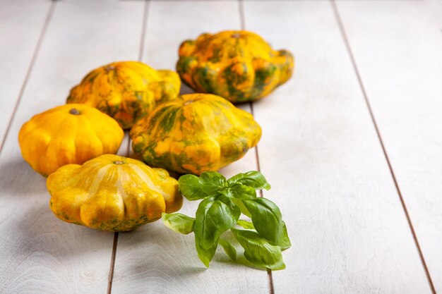 Gelbe Patissons oder Squash und ein Basilikumblatt auf hellem Holzhintergrund