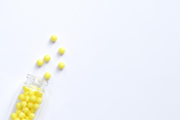Gelbe Pillen werden aus einer Glasflasche auf weißem Hintergrund mit Ascorbinsäure von oben gegossen
