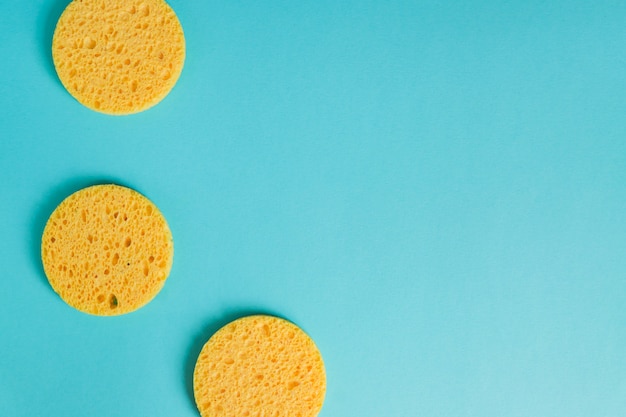 Gelbe runde Schwämme auf pastellblauem Hintergrund, Gesichtspflege. Kosmetisches Gerät. Tiefenreinigung der Haut.