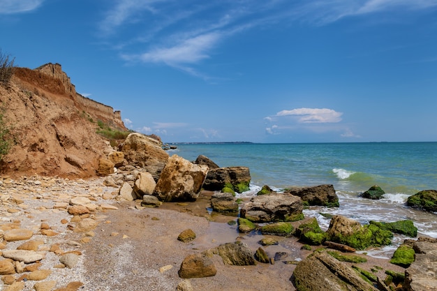 Gelbe Sandfelsen und Steine verschiedener Formen an der Schwarzmeerküste. Blauer Himmel und türkisfarbenes Wasser.