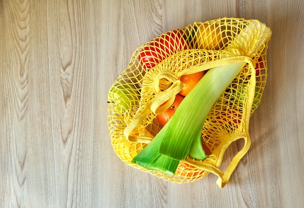 Gelbe Schnur-Einkaufstasche mit Gemüse und Früchten, die auf dem Küchentisch hängen