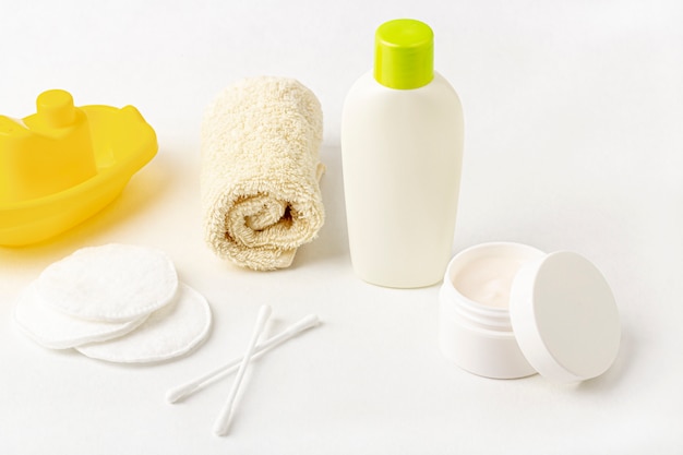 gelbe Shampooflasche, Handtuch, Wattepads und Spielzeugboot auf Weiß.