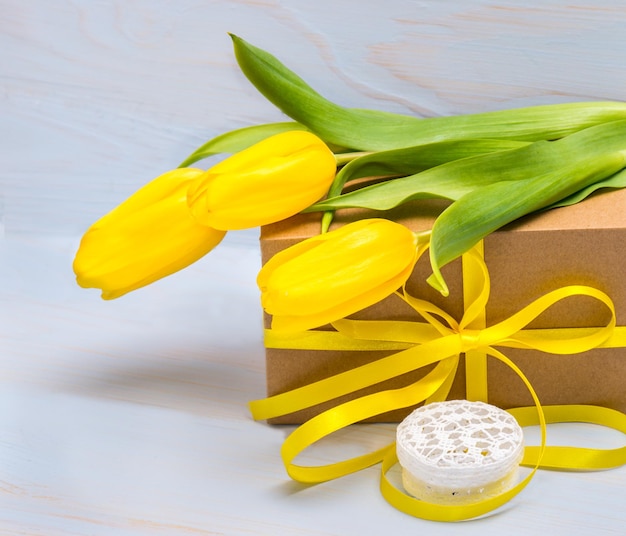 Gelbe Tulpen auf einer Geschenkbox mit Schleife und auf einem Hintergrund aus Naturholz Muttertag Valentinstag Grußkarte mit Platz für Text