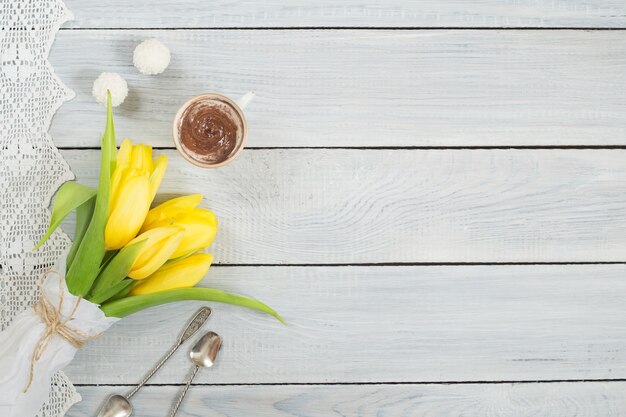 Gelbe Tulpen, Schokolade und Bonbons auf einem weißen Holztisch