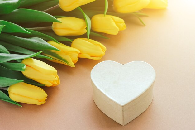 Gelbe Tulpen und Geschenkbox in Form eines Herzens auf Beige