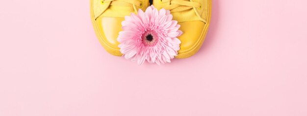 Gelbe Turnschuhe und rosafarbene Gerbera-Blume Minimales Banner mit Platz für Text in Pastellfarben