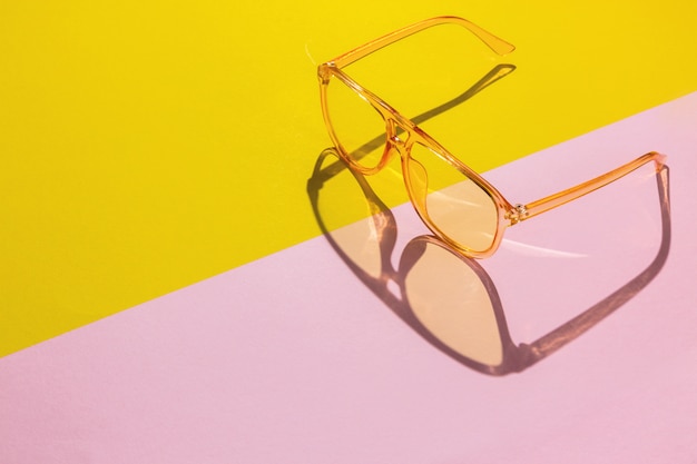 Gelbe übergroße transparente Sonnenbrille auf abstraktem rosa diagonalem Hintergrund mit Raum für Text