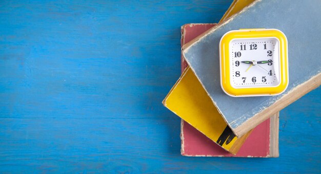 Gelbe Uhr und Bücher auf blauem Holzhintergrund