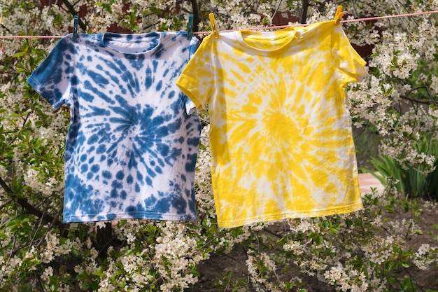 Gelbe und blaue Tie-Dye-T-Shirts hängen an einer Wäscheleine vor dem Hintergrund eines blühenden Baums
