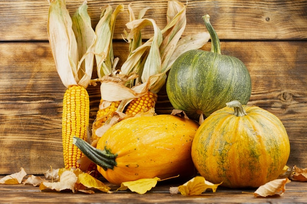 Gelbe und grüne Kürbisse mit Mais auf einem Holztisch. Herbsterntekonzept. Herbststillleben.