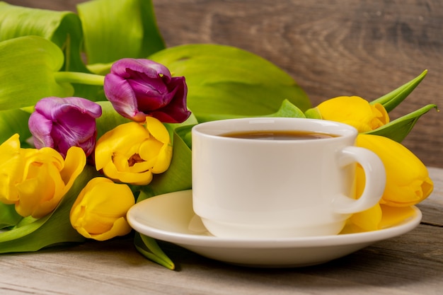 Gelbe und lila Tulpen und Kaffeetasse auf rustikalem Holztisch