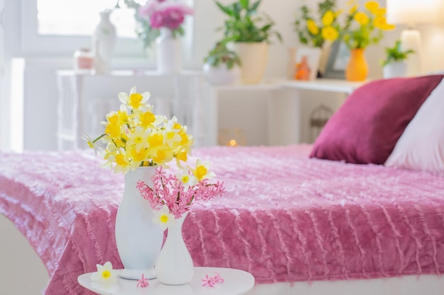 Gelbe und rosafarbene Frühlingsblumen in Vase im modernen rosafarbenen Schlafzimmer