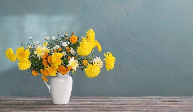 Gelbe und weiße Chrysantheme im weißen Krug auf Holztisch